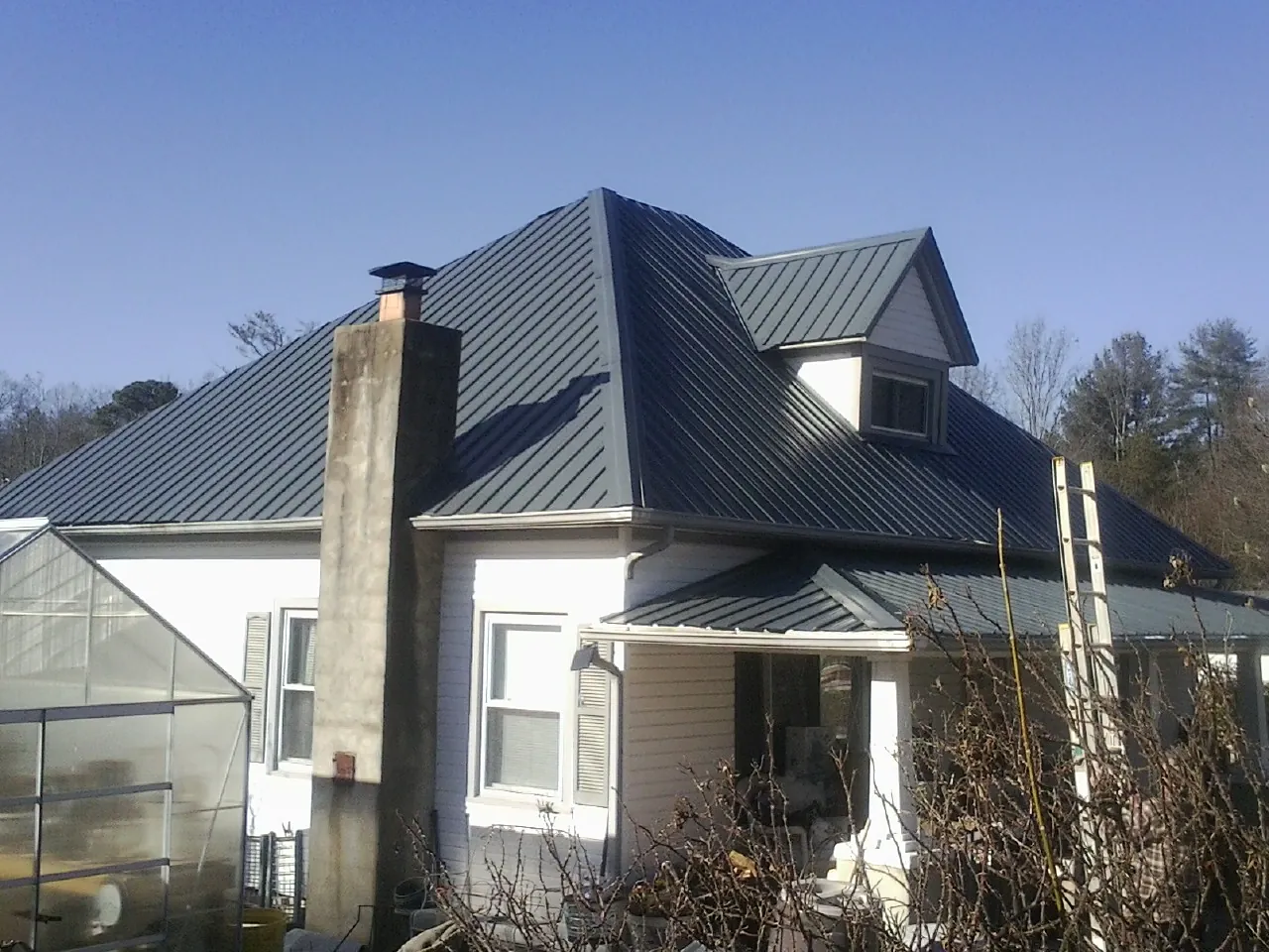 Dark blue standing seam metal roof on a white farmhouse with dormer — Slate & Tile Roof Repair by Roofing Brothers in Rodeo