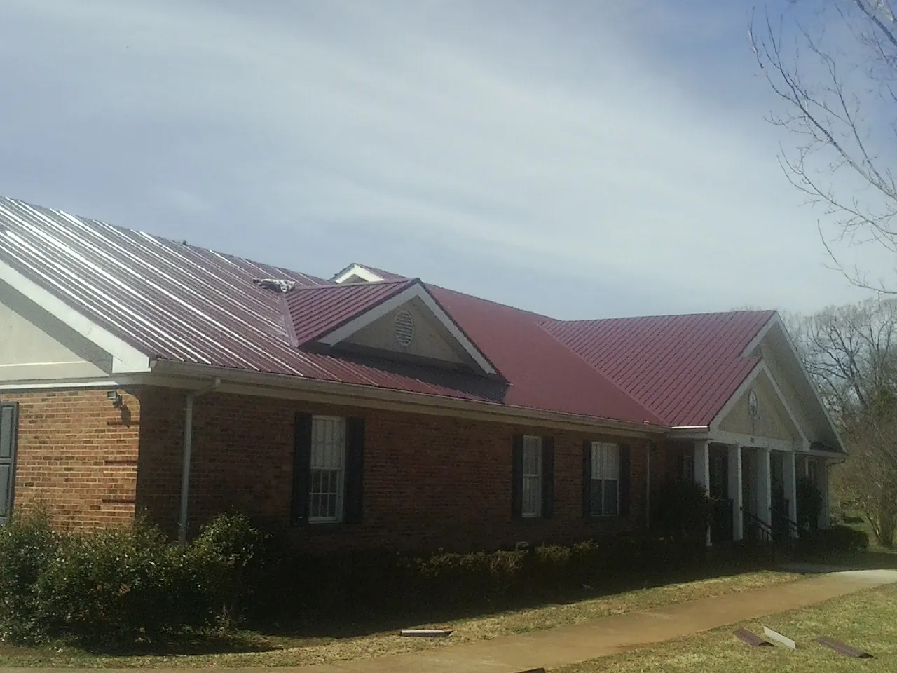 Red metal roof with gabled entries on a long brick building, from a Hail Damage Roof Repair job in Rodeo