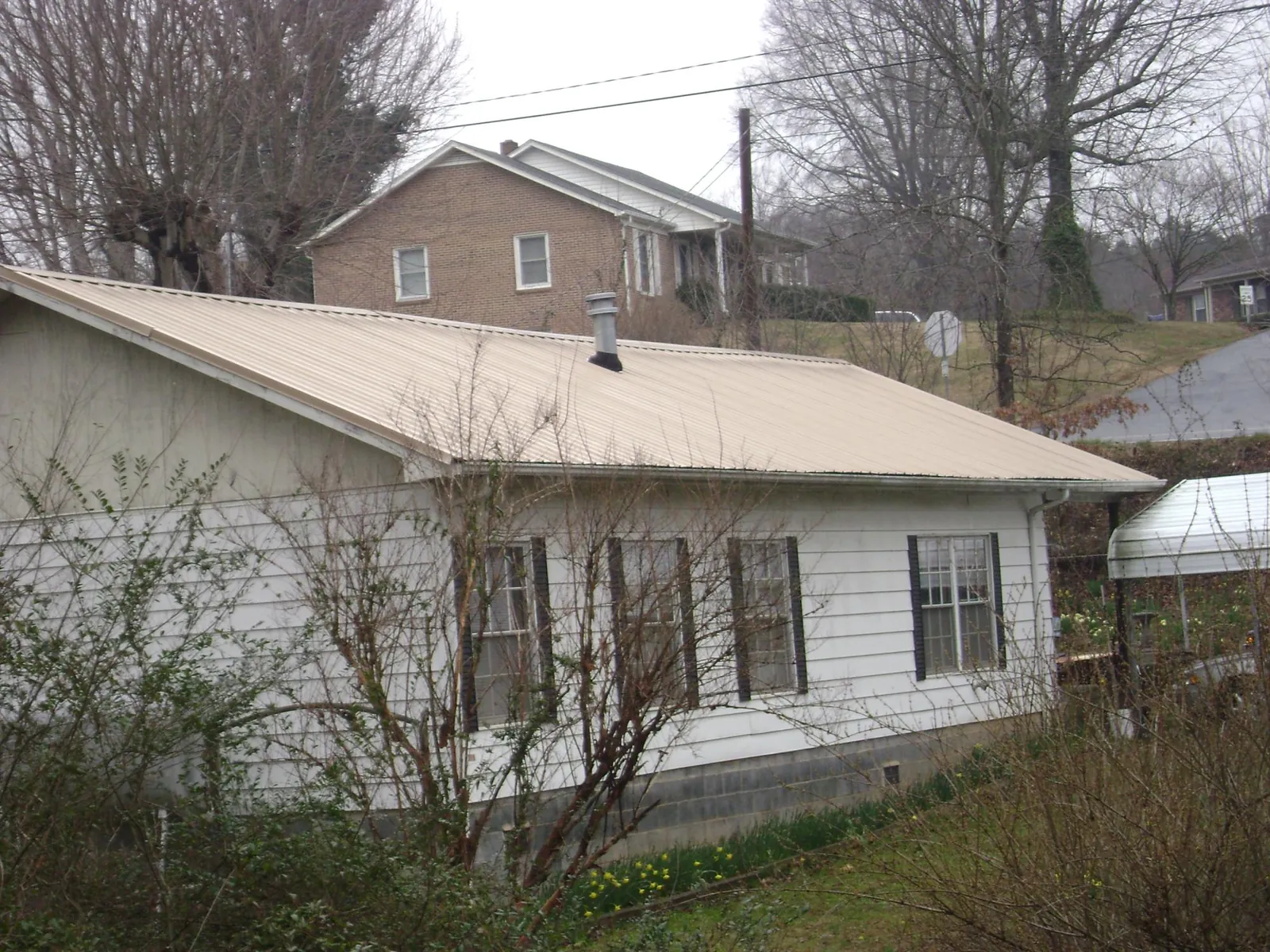 Tan metal roof on a white sided house set into a hillside — Commercial Roofing by Roofing Brothers in Rodeo